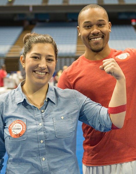 Two people with red bandage around arm flexing biced and smiling.