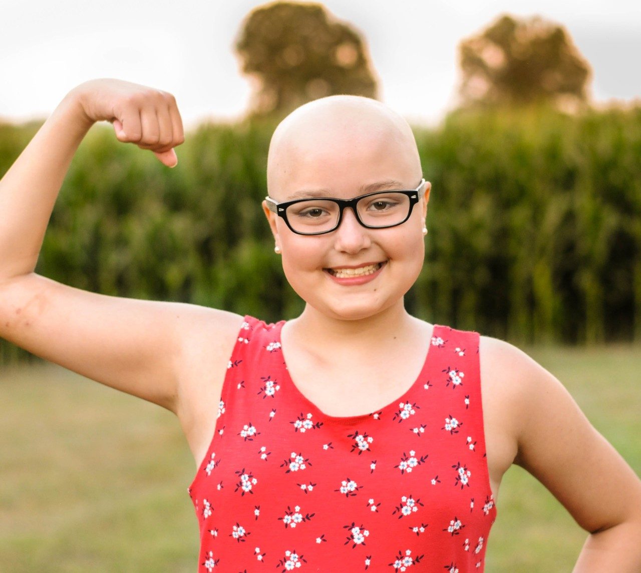 Youngster with shaved head, wearing glasses, smiling and flexing arm.