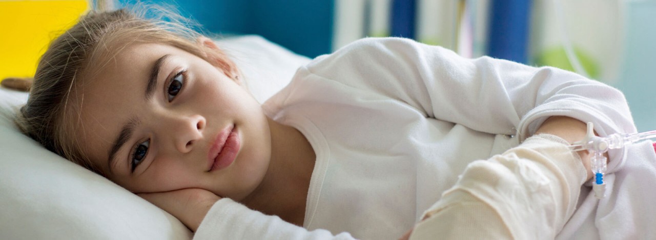 Child laying in hospital bed with hand wrapped in cloth and IV in hand.